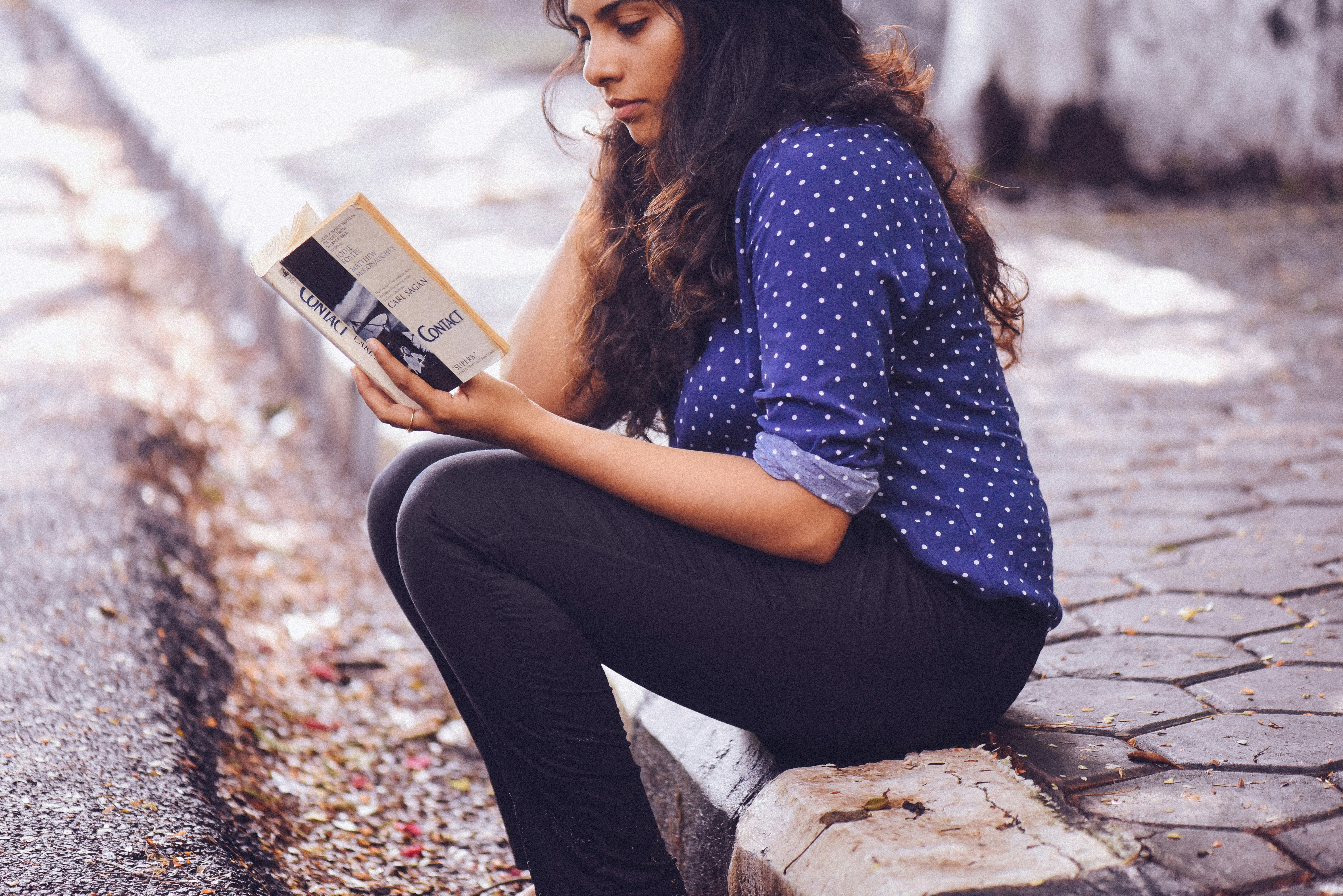 woman sitting on gutter reading book